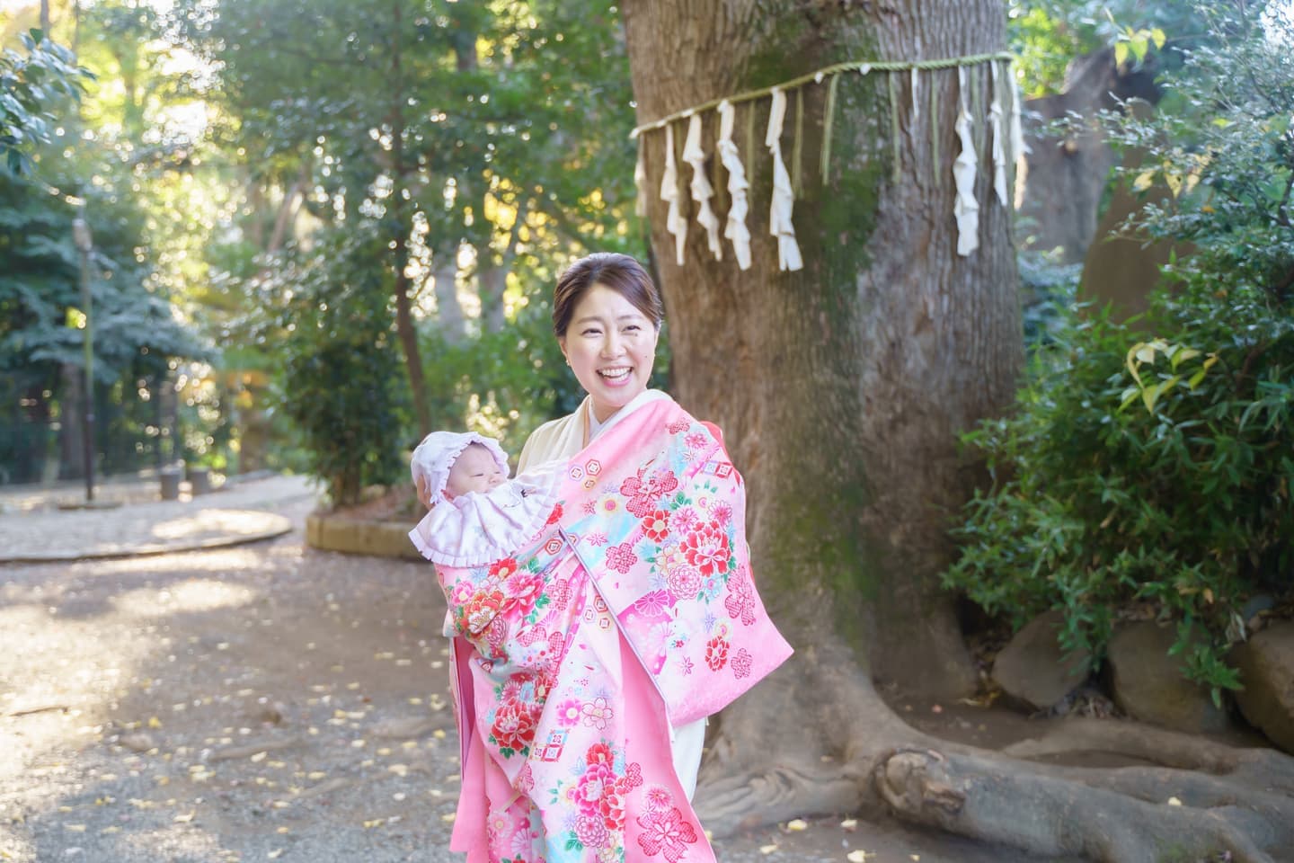 代々木八幡宮の御神木の前でお宮参りの赤ちゃんを抱っこする着物姿のママの写真